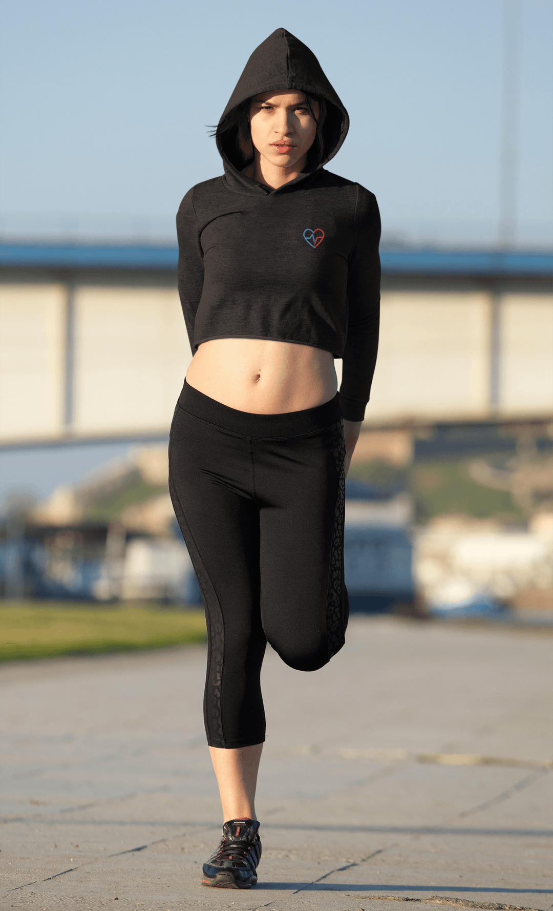 Woman stretching in a Love Clan black cropped hoodie and leggings near the water