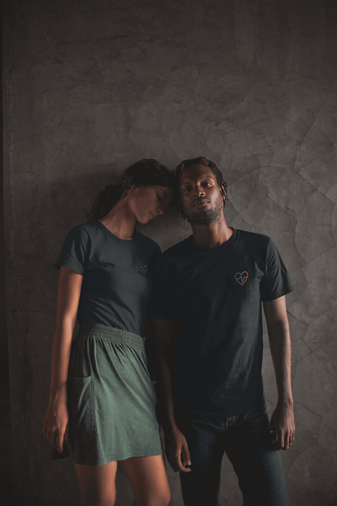 A couple leaning against a wall  while wearing the Love Clan Classic Embroidered T-Shirt by Norian Love