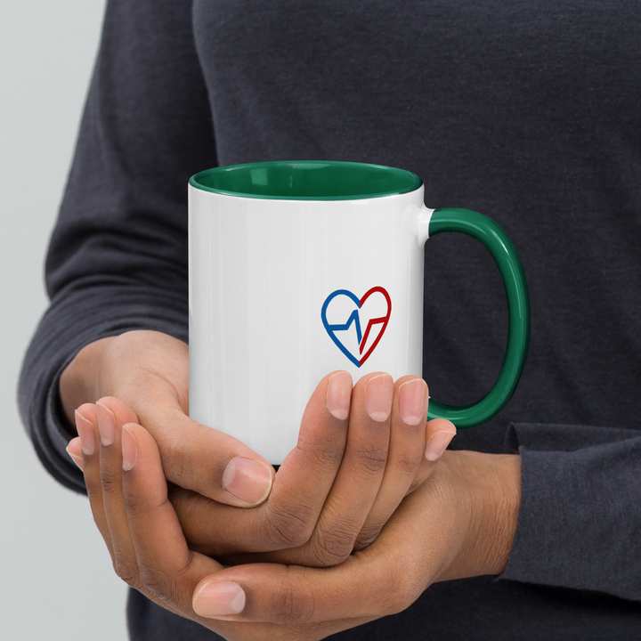 Person holding a white mug with a green interior and handle, featuring a blue and red heart design.