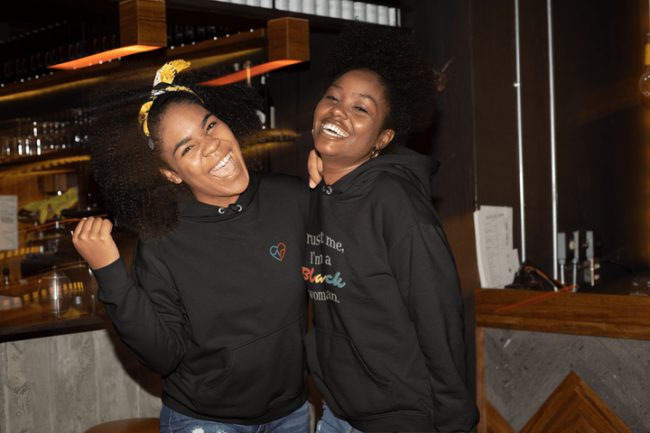 Two women out on the town, laughing.  One is wearing the Love Clan Classic Embroidered Hoodie by Norian Love