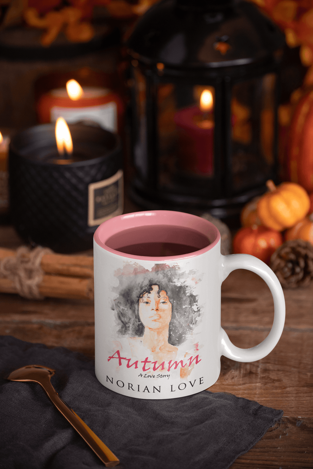 White mug with pink interior featuring the Autumn cover artwork, displayed with fall-themed candles and seasonal decor.