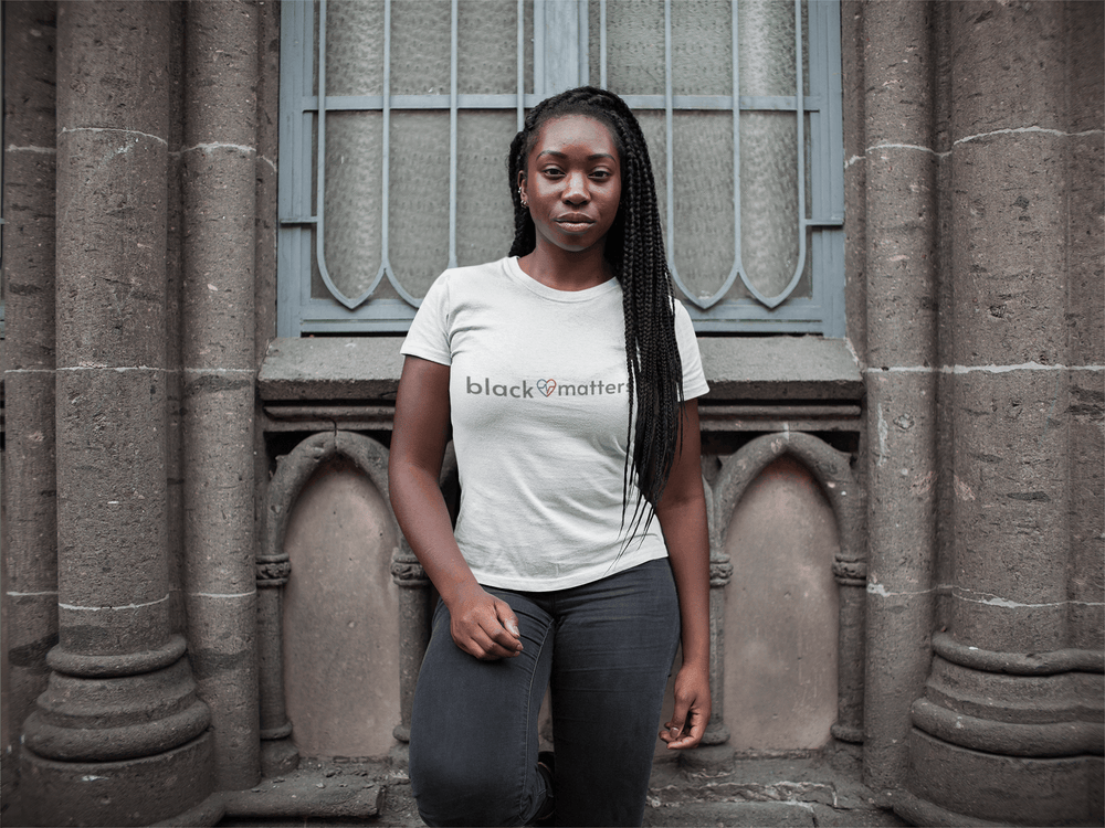 Black woman, with braids wearing a Black Love Matters shirt, standing outside a church building