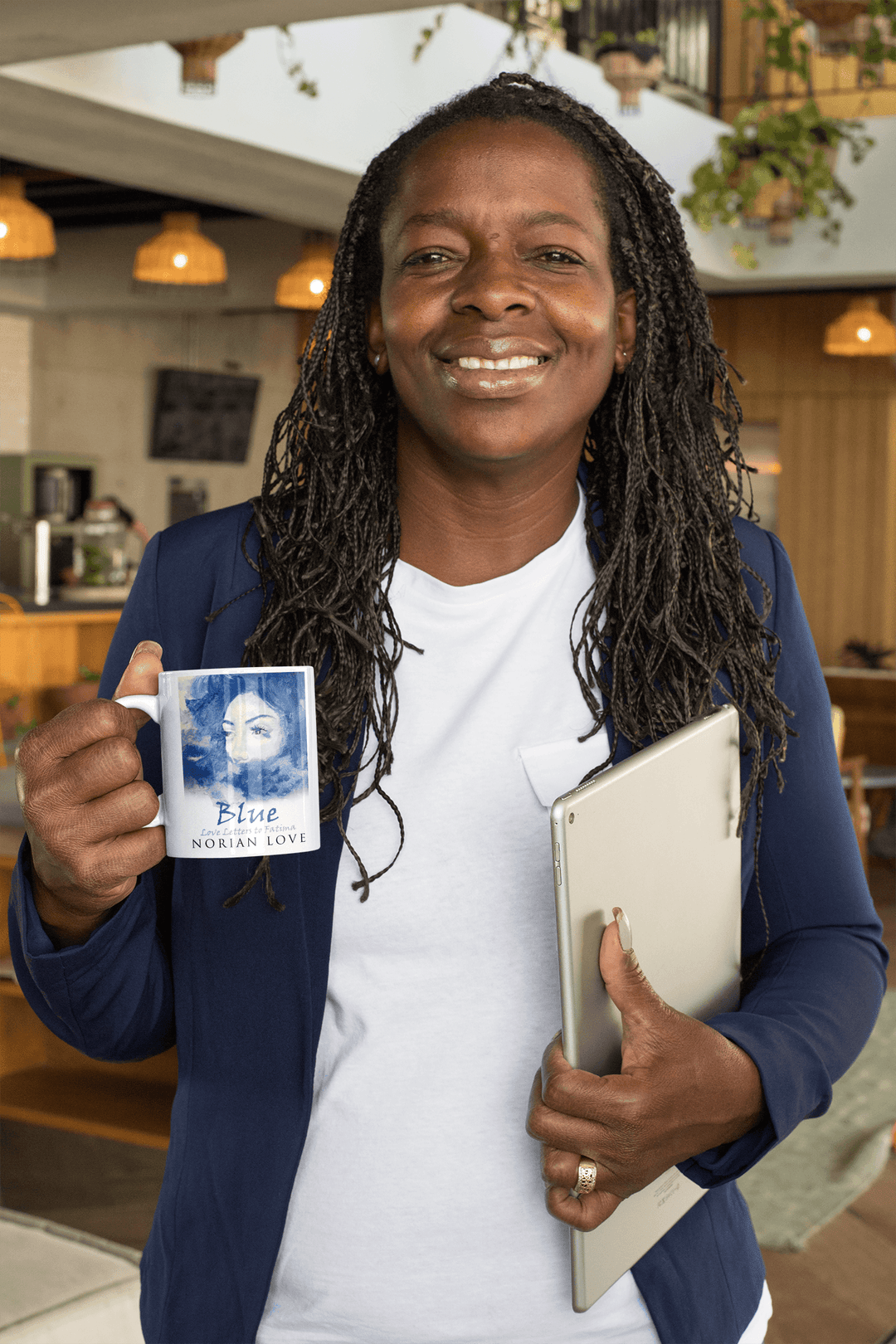 Smiling woman at a workspace holding the Blue Love mug with Norian Love cover art.