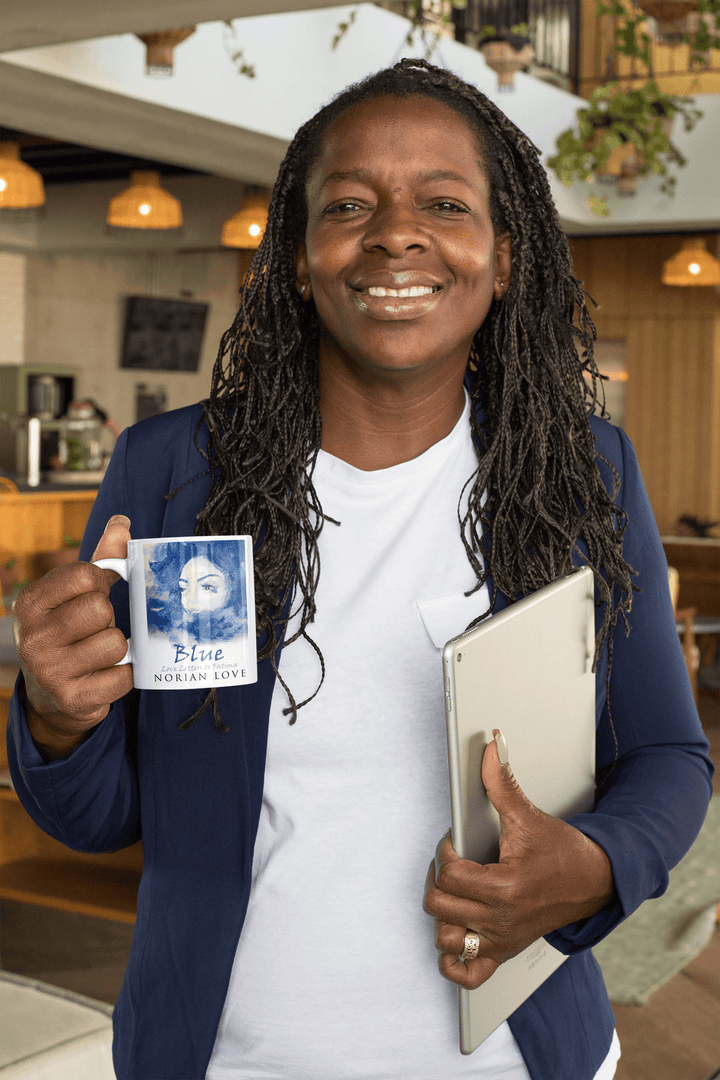 Smiling woman at a workspace holding the Blue Love mug with Norian Love cover art.