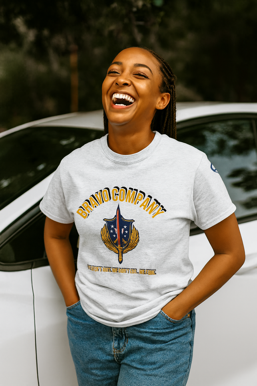 Black woman wearing an ash gray Bravo Company shirt laughing while leaning against a car