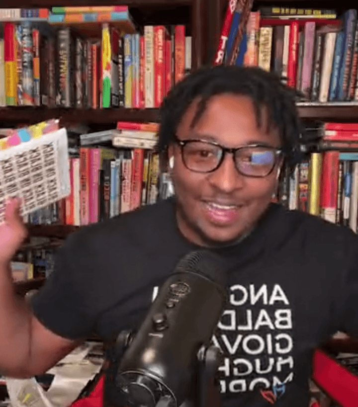 Black man in GOATS T-Shirt speaking in front of microphone, showcasing pride in Black literature icons.