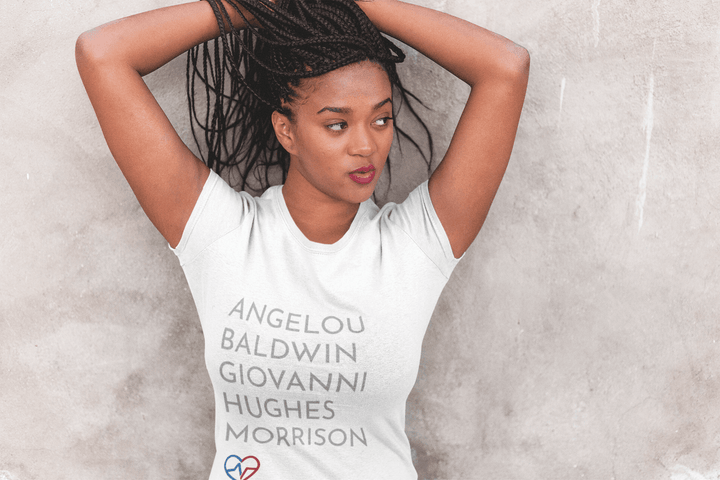 Young Black woman wearing GOATS T-Shirt leaning against wall, celebrating Black authors and culture.