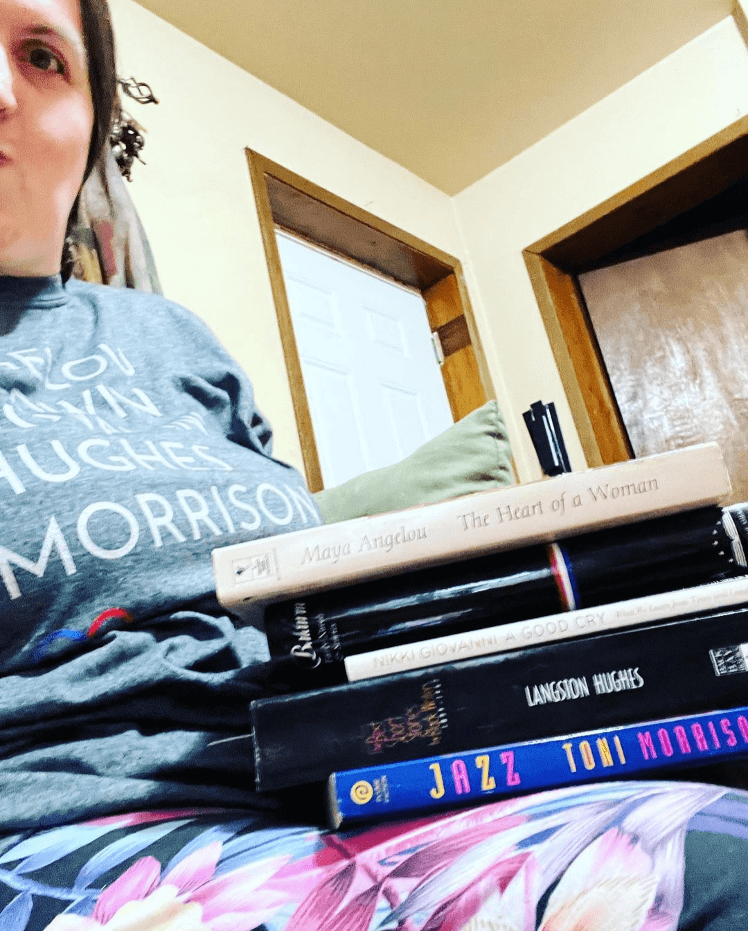 Woman wearing GOATS T-Shirt paired with books by Maya Angelou, Nikki Giovanni, Langston Hughes, and Toni Morrison.