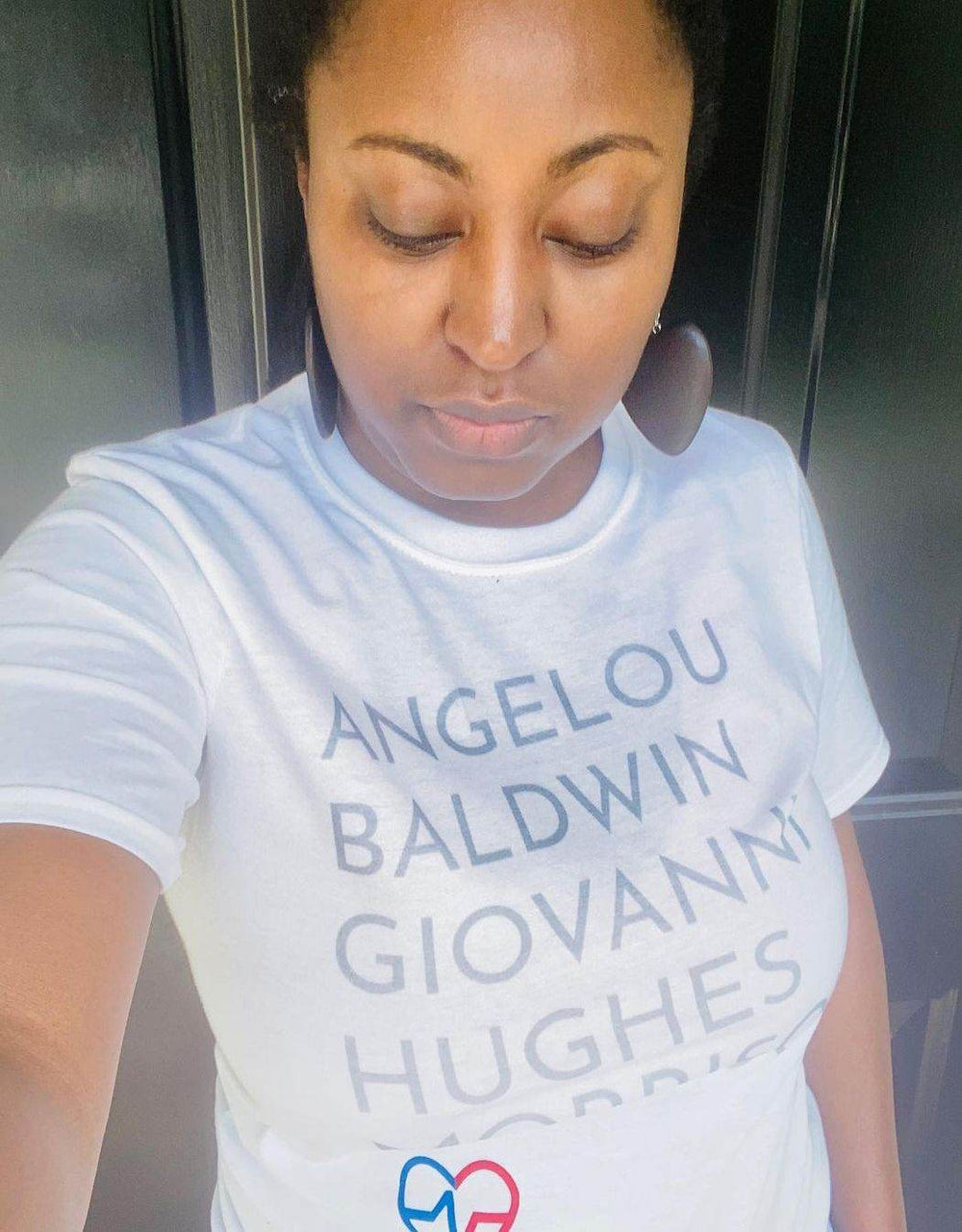 Woman taking selfie in white GOATS T-Shirt featuring legendary Black authors Angelou, Baldwin, Giovanni, Hughes, and Morrison.