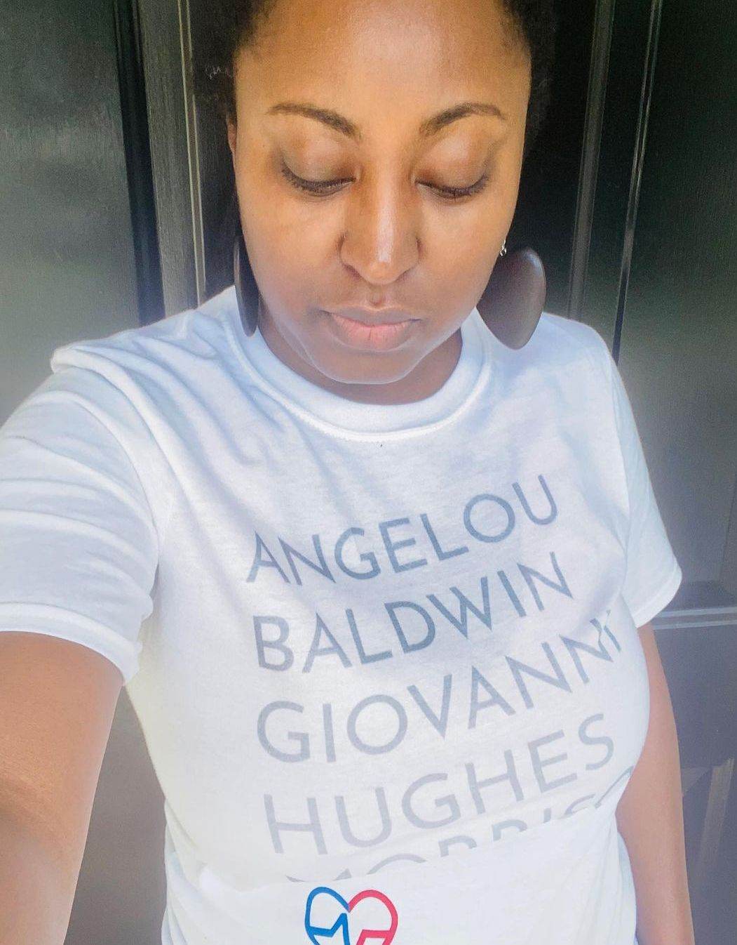 Woman taking selfie in white GOATS T-Shirt featuring legendary Black authors Angelou, Baldwin, Giovanni, Hughes, and Morrison.