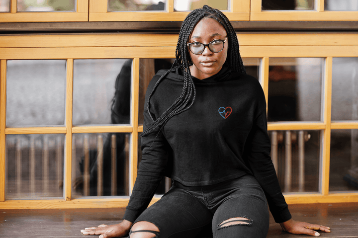 Black woman in glasses wearing Love Clan black crop top hoodie sitting by a window