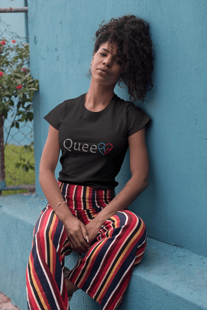 Black woman wearing the Love Is Queen shirt leaning against a blue wall.