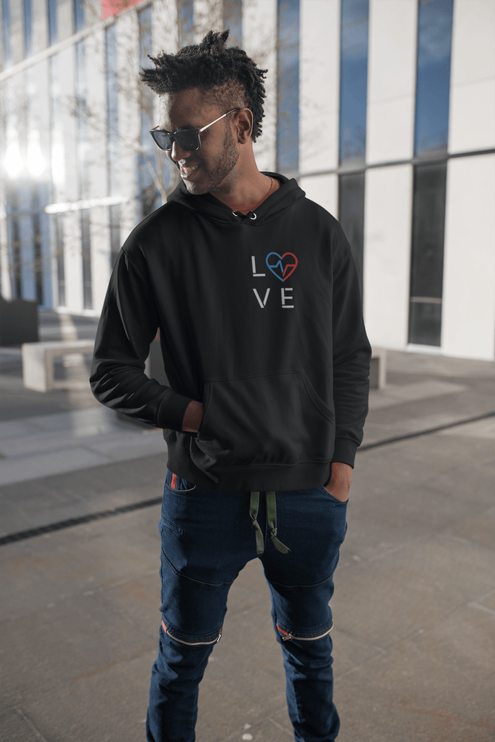 Black man wearing the Love Season Hoodie featuring the red and blue Love Clan emblem on a black hoodie, standing outdoors in a modern urban setting.