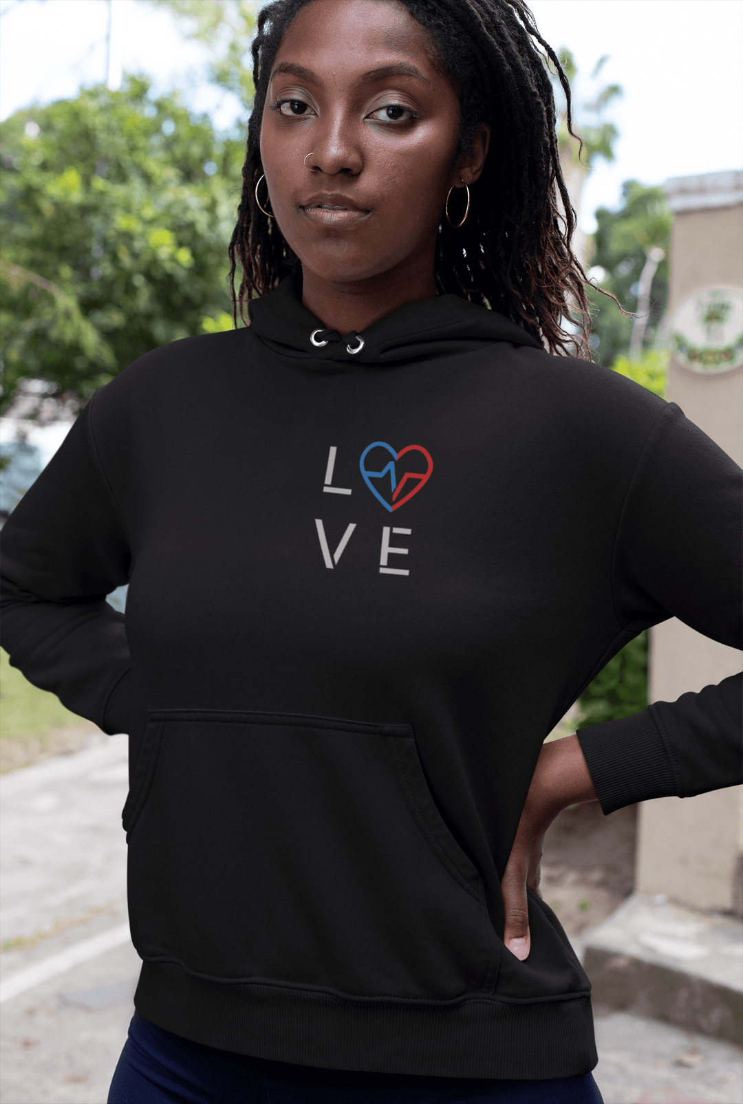 Black woman wearing the black Love Season Hoodie with the red and blue Love Clan emblem, photographed outdoors in a clean, modern streetwear look.
