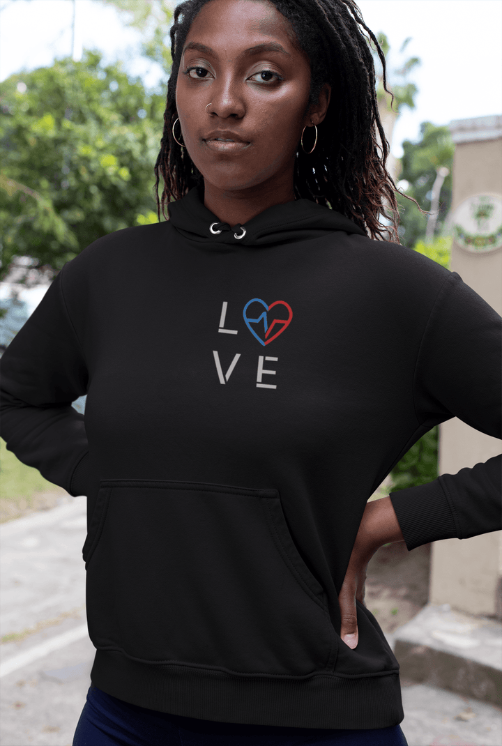 Black woman wearing the black Love Season Hoodie with the red and blue Love Clan emblem, photographed outdoors in a clean, modern streetwear look.