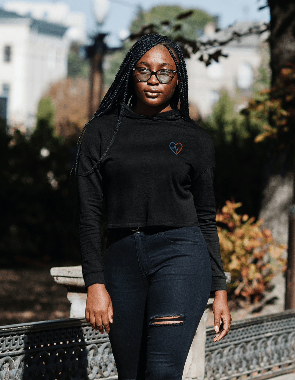 Black woman with braids wearing Love Clan black crop hoodie and jeans walking outside
