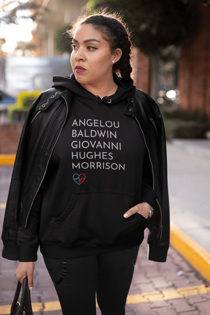Black woman in streetwear style wearing the GOATs Hoodie with names of Black literary legends Angelou, Baldwin, Giovanni, Hughes, and Morrison.