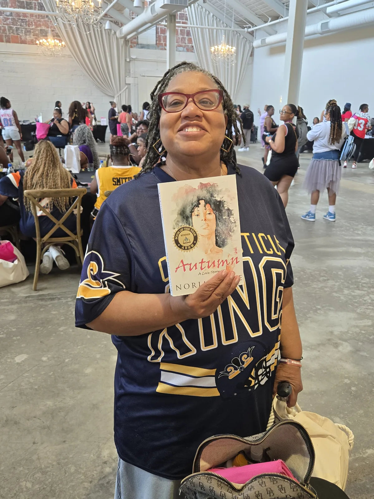 A smiling reader holding Autumn: A Love Story at a book gathering.